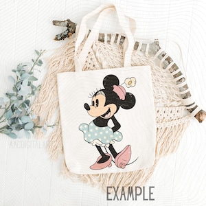 K&ouml;nnte beinhalten: Eine wei&szlig;e Tragetasche mit einer Vintage-Illustration von Minnie Mouse. Minnie tr&auml;gt ein blaues Polka-Dot-Kleid, rosa Schuhe und eine passende Schleife. Das Wort "EXAMPLE" ist unten auf der Tasche aufgedruckt.