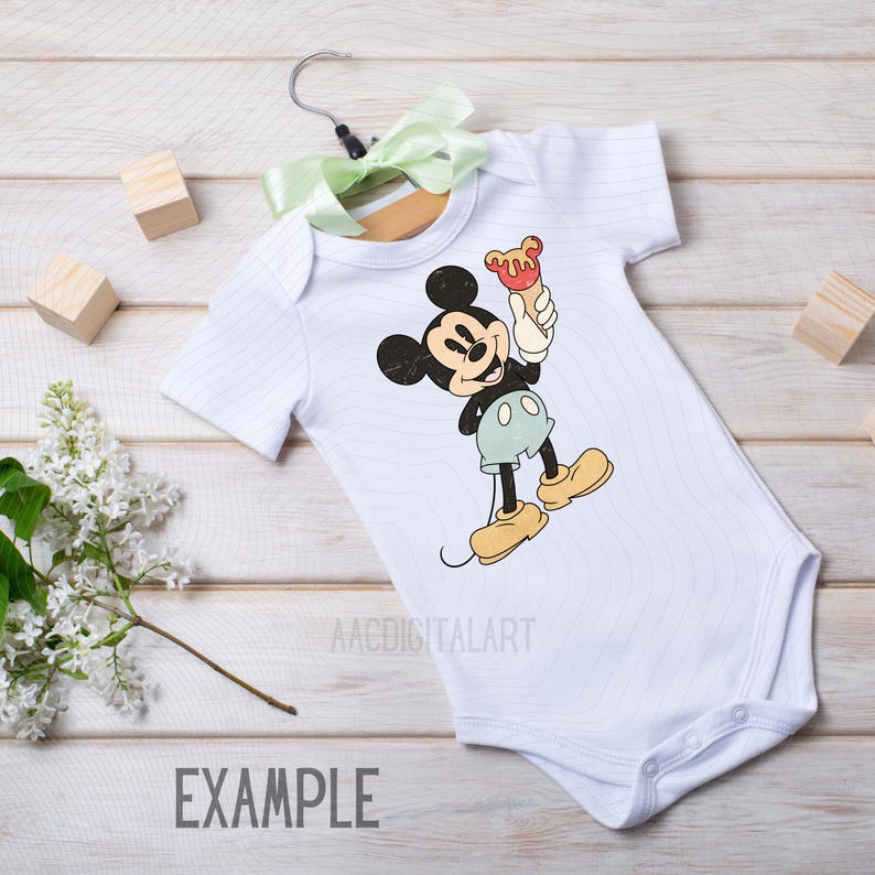 K&ouml;nnte beinhalten: Wei&szlig;er Baby-Body mit einem Mickey Mouse-Design, das ein Eis am Stiel h&auml;lt. Der Body h&auml;ngt an einem Holzkleiderb&uuml;gel mit einer gr&uuml;nen Schleife. Das Wort "EXAMPLE" ist unten aufgedruckt.
