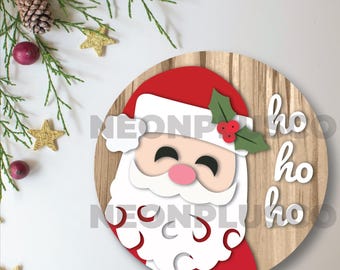 May include: A round wooden ornament with a paper cutout of Santa Claus's face and the words "ho ho ho" written in white. The ornament has a wood grain pattern and a red and white Santa hat.