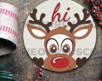 May include: A round, white bauble with a cartoon reindeer face. The reindeer has brown antlers, brown eyes, a red nose, and a brown face. The word "hi" is written in red letters on the bauble.
