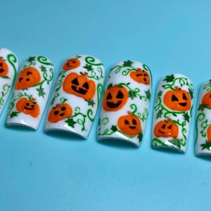 May include: Ten white fake nails with a Halloween theme. Each nail is decorated with green vines and orange jack-o'-lantern pumpkins.