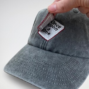 K&ouml;nnte beinhalten: Eine graue Baseballkappe mit einem kleinen, wei&szlig;en Patch, auf dem in schwarzen Buchstaben "Once upon a time" steht.