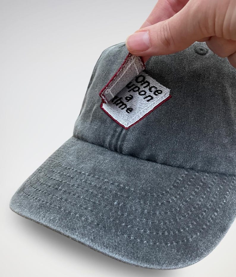 K&ouml;nnte beinhalten: Eine graue Baseballkappe mit einem kleinen, wei&szlig;en Patch, auf dem in schwarzen Buchstaben "Once upon a time" steht.