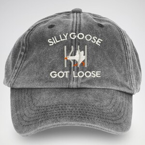 May include: A black distressed baseball cap with white embroidery that reads "Silly Goose Got Loose". The embroidery also includes a cartoon image of a white goose escaping from a fence.