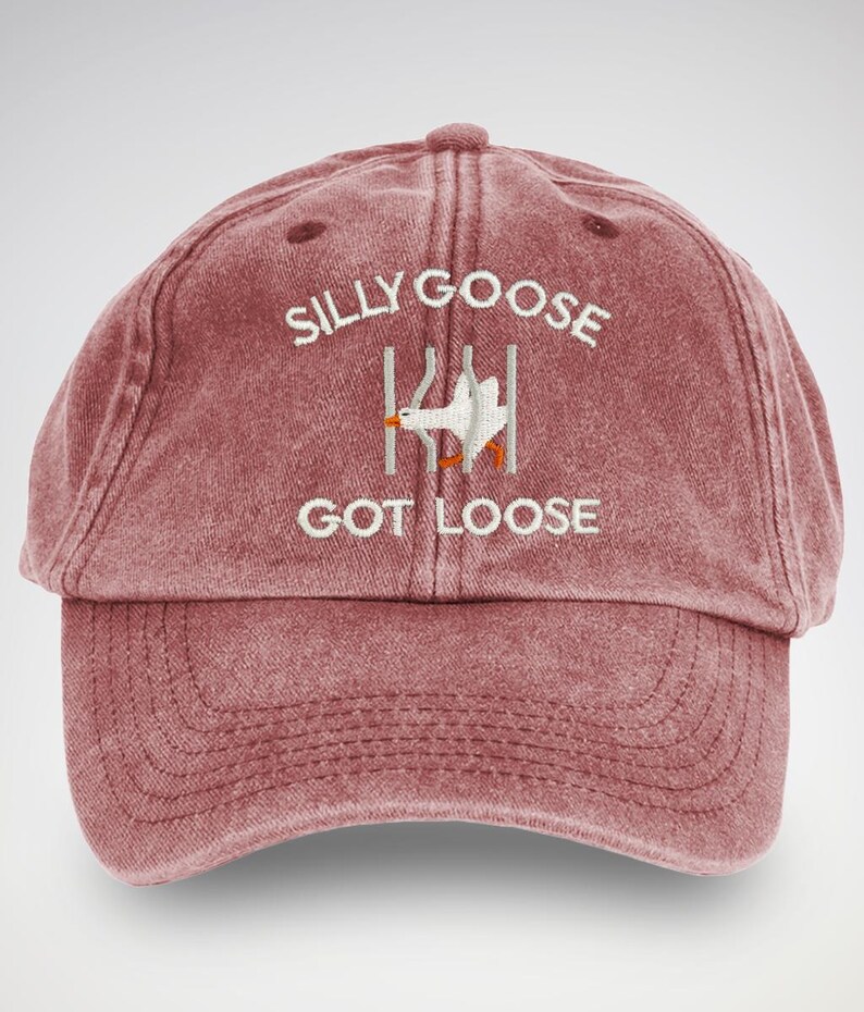 May include: A red vintage-style baseball cap with the text "Silly Goose Got Loose" embroidered in white. A white goose is also embroidered on the cap, appearing to be escaping from a fence.