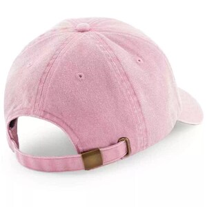 K&ouml;nnte beinhalten: Eine rosafarbene Baseballkappe mit einem braunen verstellbaren Riemen. Die Kappe hat einen leicht abgenutzten Look.