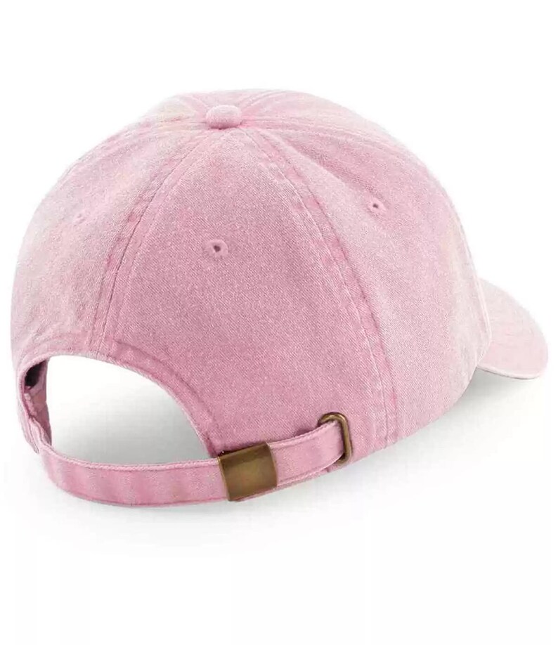 K&ouml;nnte beinhalten: Eine rosafarbene Baseballkappe mit einem braunen verstellbaren Riemen. Die Kappe hat einen leicht abgenutzten Look.