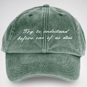 Può includere: Un cappello da baseball in cotone verde consumato con testo ricamato in bianco che recita "Try to understand before one of us dies."