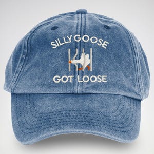 May include: A blue denim baseball cap with white embroidery that reads "Silly Goose Got Loose". A white goose is depicted escaping from a fence.