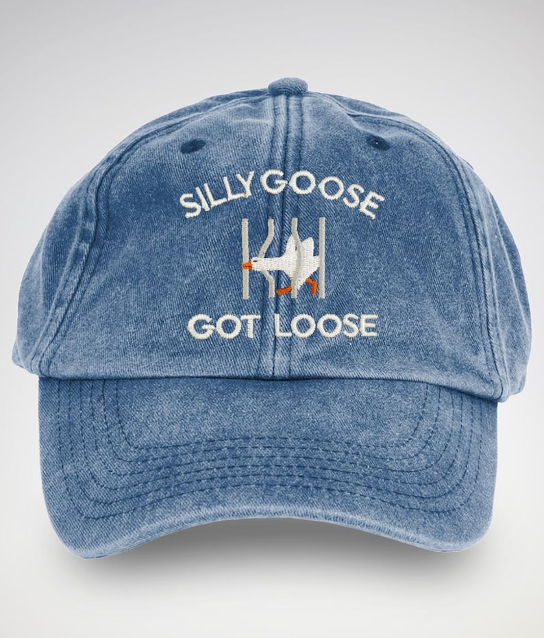 May include: A blue denim baseball cap with white embroidery that reads "Silly Goose Got Loose". A white goose is depicted escaping from a fence.