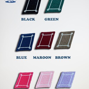 K&ouml;nnte beinhalten: Neun gestickte B&uuml;gelbilder in verschiedenen Farben, jedes mit einer wei&szlig;en umrandeten Diamantform mit wei&szlig;em Rand. Die Farben sind Schwarz, Gr&uuml;n, Blau, Rotbraun, Braun, Pink, Hellrosa und Lila.