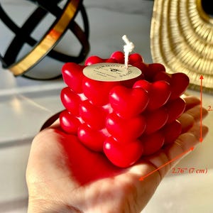 May include: Red heart-shaped candle with a white wick. The candle is 2.76 inches wide and 2.36 inches tall.