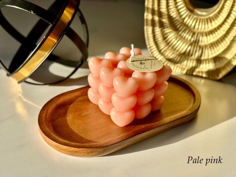 May include: Pale pink heart-shaped candle on a wooden tray. The candle is made of multiple hearts stacked on top of each other. The label on the candle says "remarkable".