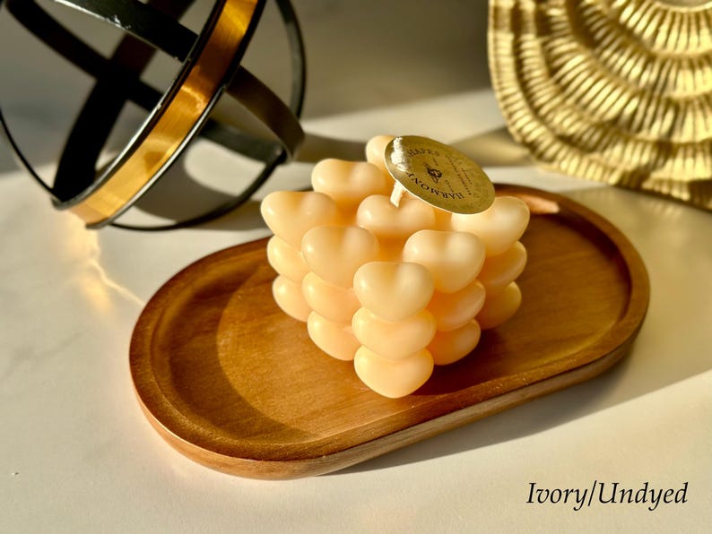 May include: A heart-shaped candle in ivory, arranged in a cube shape, sits on a wooden tray. The candle is uncolored and has a label that reads "Bath & Body Works".