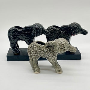 May include: Three ceramic sheep planter figurines. Two are black and one is gray with a swirl pattern. The sheep are standing on a black wooden base.
