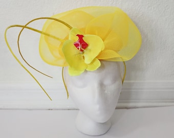 May include: A yellow mesh hat with a yellow flower and red center. The hat is on a white mannequin head.