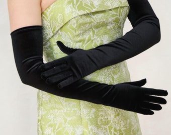 May include: A pair of long black satin gloves. The gloves are worn by a person wearing a green and white floral dress.