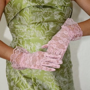 May include: A woman wearing a green strapless dress with a white floral pattern and pink lace gloves.
