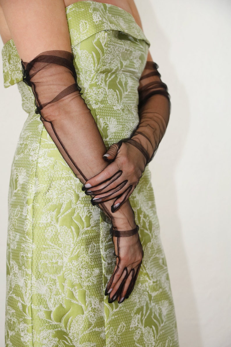May include: A woman wearing a green and white floral strapless dress with black sheer gloves.