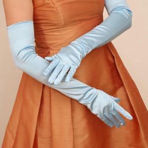 May include: Pale blue satin opera gloves. The gloves are long, reaching past the elbows, and have a smooth, shiny texture. The gloves are paired with a rust-coloured dress.