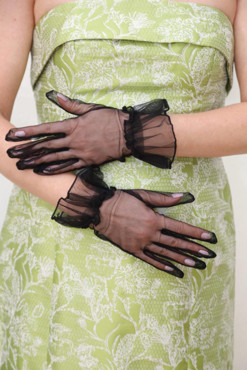May include: A pair of black sheer gloves with ruffled edges. The gloves are made of a delicate, lightweight fabric and have a classic, elegant design.