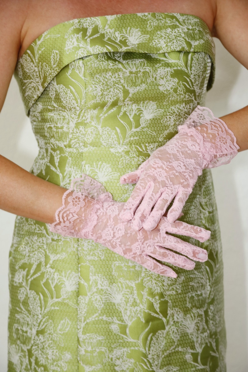 May include: A strapless green dress with a white floral pattern and a pair of pink lace gloves.