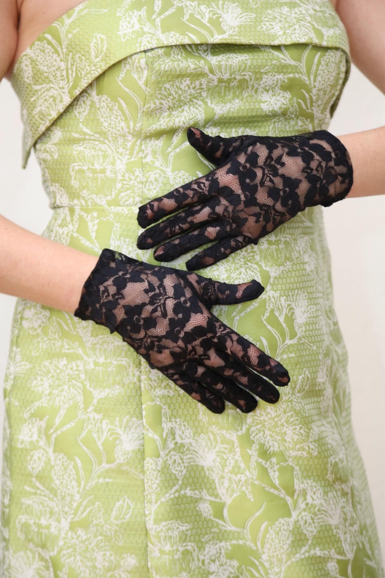 May include: A pair of black lace gloves with a floral pattern. The gloves are on a green background with a white floral pattern.