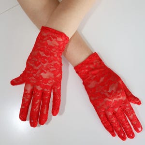 May include: A pair of vibrant red lace gloves. The gloves are crafted from a delicate, floral-patterned lace fabric. The gloves are displayed against a white backdrop.