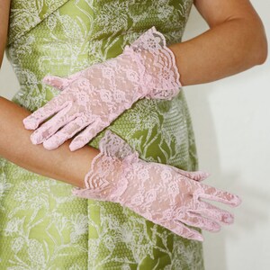 May include: A pair of pink lace gloves with a floral pattern. The gloves are worn by a person wearing a green dress with a floral pattern.
