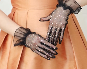 May include: A pair of black sheer gloves with a ruffled cuff and rhinestones. The gloves are worn on a person's hands.