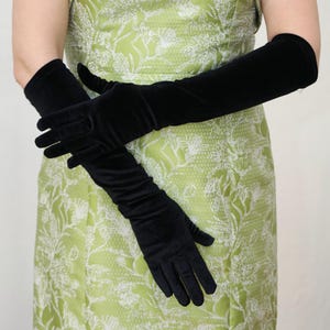 May include: A woman wearing a green floral dress and long black velvet gloves.