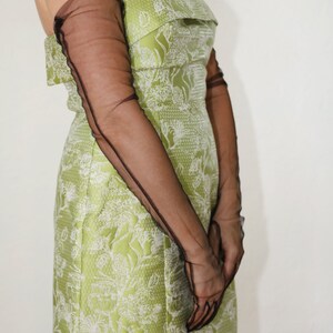May include: A strapless green dress with a white floral pattern and black sheer long gloves.