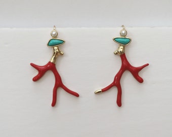 Puede incluir: Un par de pendientes con diseño de coral rojo con detalles dorados. Cada pendiente tiene una piedra turquesa y una pequeña perla. Fondo blanco.