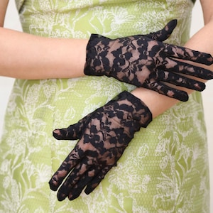 May include: A pair of black lace gloves with a floral pattern. The gloves are worn by a person wearing a green dress with a floral pattern.