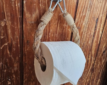 May include: A rustic toilet paper holder made of thick, twisted rope and metal hardware. The rope is wrapped around the metal supports and forms a loop to hold a roll of white toilet paper. The holder is mounted on a wooden surface.