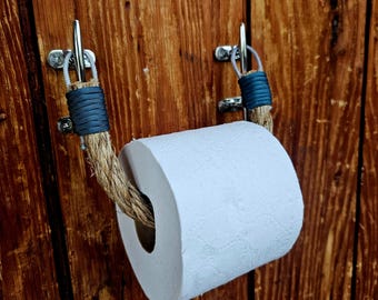 May include: A rustic toilet paper holder made of rope and metal, mounted on a wooden surface. The rope is wrapped with blue twine at the mounting points. A roll of white toilet paper is in place.