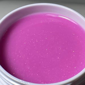 May include: A small jar of pink nail polish with a shimmery finish.