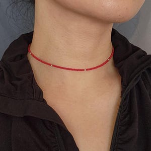 Może przedstawiać: Czerwony naszyjnik choker z koralikami srebrnymi.