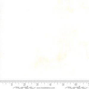 May include: White fabric with subtle yellow-beige shading. A ruler is printed along the bottom edge, with the word "moda" repeated. The website address www.modafabrics.com is also visible. This fabric is suitable for quilting and sewing projects.