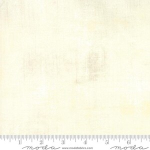 May include: Off-white fabric with a textured surface. The material has a creamy tone with subtle variations, giving it a vintage or worn appearance. A ruler is at the bottom with the word "moda" and the website address.