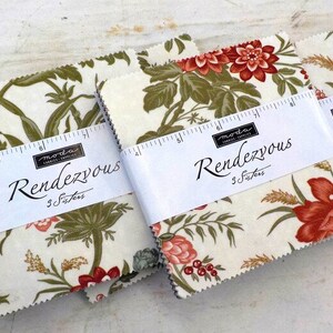 May include: Fabric squares with floral patterns in red, green, and cream. The fabric bundles are wrapped with white bands that read "Rendezvous" and "3 Sisters". The fabric has a vintage aesthetic.