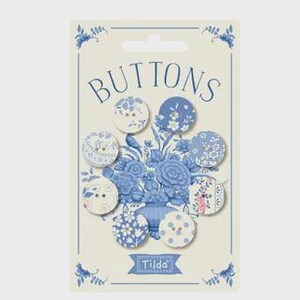 May include: A pack of eight round buttons featuring various blue and white floral and geometric patterns. The packaging is cream-coloured with blue floral illustrations, the word BUTTONS at the top, and the brand name Tilda at the bottom.