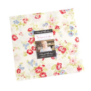 May include: A square of fabric featuring a floral design in red, blue, and pink hues against a cream backdrop. A small card with "moda" and "Hollyhock & Roses" text rests on the fabric. Suitable for sewing or quilting.