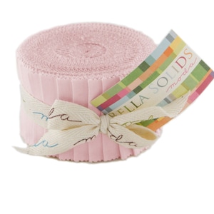 May include: A roll of pale pink fabric strips, secured with a cream ribbon. A colourful tag with the words "BELLA SOLIDS moda" is attached. The fabric is tightly rolled, suggesting it is unused.