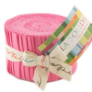 May include: A roll of pink fabric strips, secured with a cream ribbon tied in a bow. A tag with the text "LA SOLIDS moda" is attached. The fabric is a solid pink colour. The roll is tightly wound.