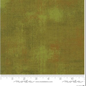 May include: Close-up of a fabric with a textured, mottled appearance. The color palette includes shades of olive green, brown, and touches of orange. The fabric has a rustic, distressed look, with visible brushstroke-like patterns.