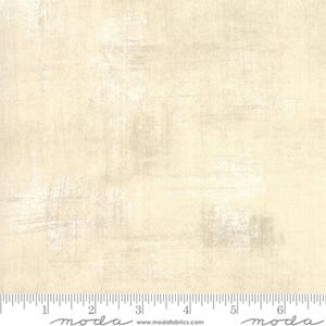 May include: Cream-coloured fabric with a textured, distressed appearance. The fabric has subtle variations in tone, with lighter and darker areas creating visual depth. The surface shows brushstroke-like markings, adding to the vintage aesthetic. Suitable for quilting and craft projects.