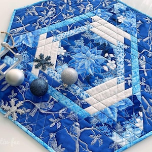 Könnte beinhalten: Sechseckiger, blau gesteppter Tischläufer mit Winterblumen- und Vogeldesign. Der Läufer hat weiße und hellblaue Akzente, mit dekorativen Ornamenten und einem Miniatur-Schlitten. Der Text "Kreativ-fee" ist sichtbar.