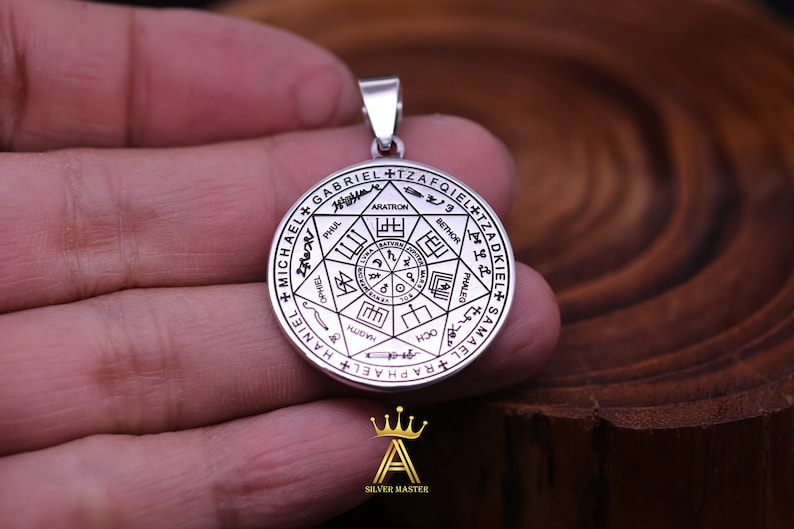 May include: Silver pendant with a circular design featuring a seven-pointed star with the names of archangels inscribed around it. The names include Michael, Gabriel, Raphael, Uriel, Zadkiel, Jophiel, and Samael.