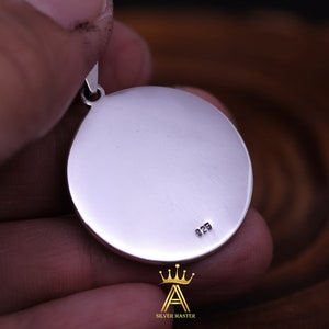 May include: A silver pendant with a round, smooth surface. The back of the pendant has the number "925" engraved on it.
